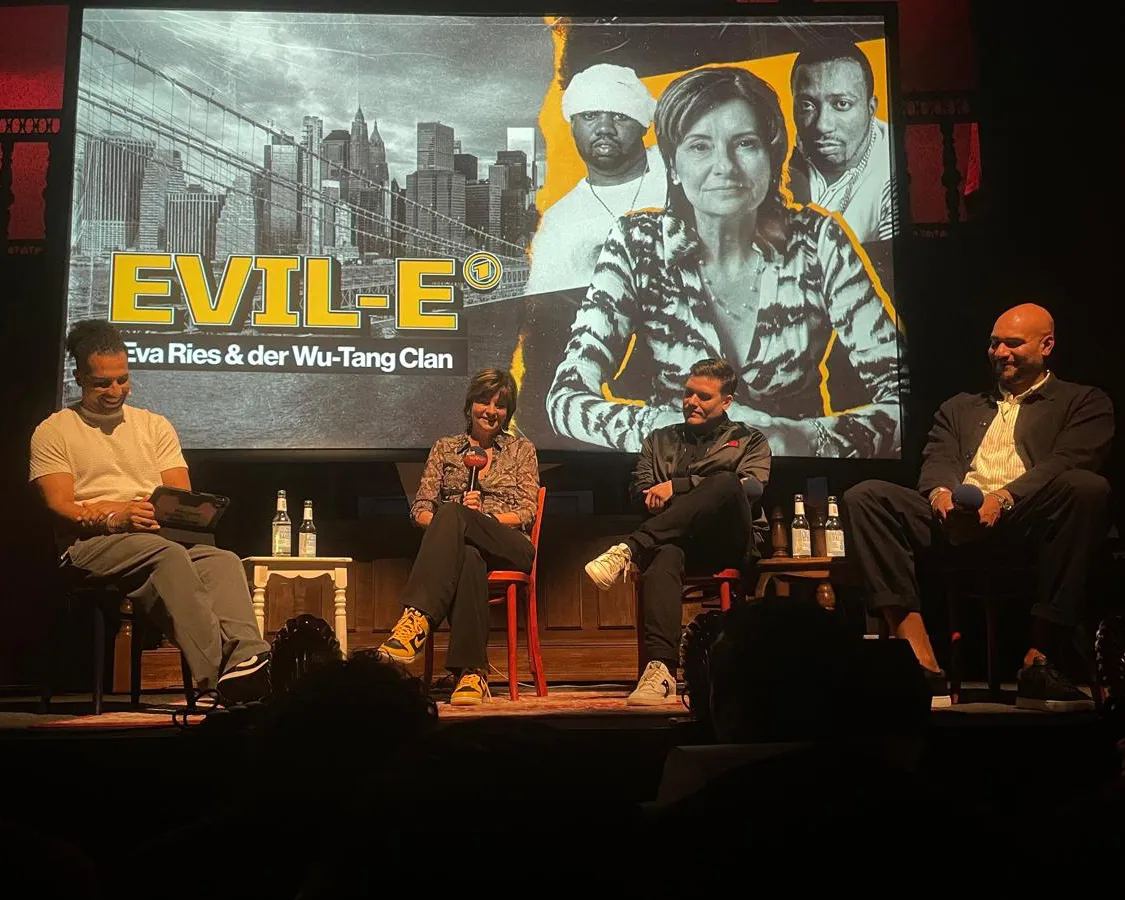 Eva Ries, Speakerin und Kulturjournalistin, sitzt auf einer Bühne und spricht bei einer Veranstaltung zum Thema Wu-Tang Clan und Hip-Hop-Kultur